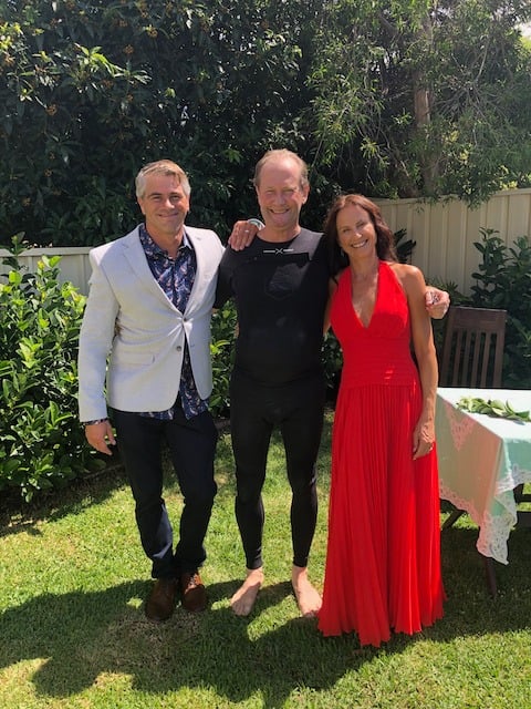 Philip in a wetsuit with the couple Vanessa and Nick in a backyard on their wedding day