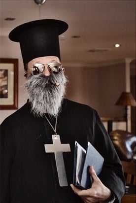 Philip dressed as a Greek Orthodox priest with kalimavkion hat and beard holding incense
